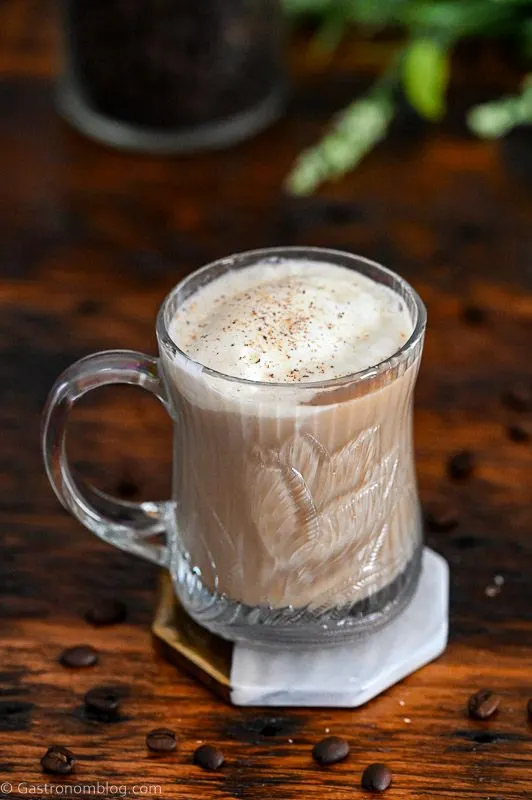 creamy light brown Nutty Irishman cocktail in glass mug with whipped cream on top. Greenery behind.