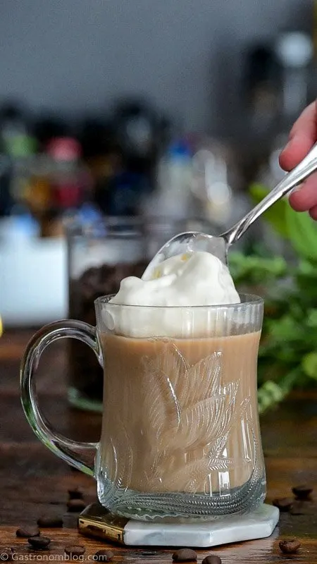 whip cream being placed on top of creamy Nutty Irishman cocktail in glass mug