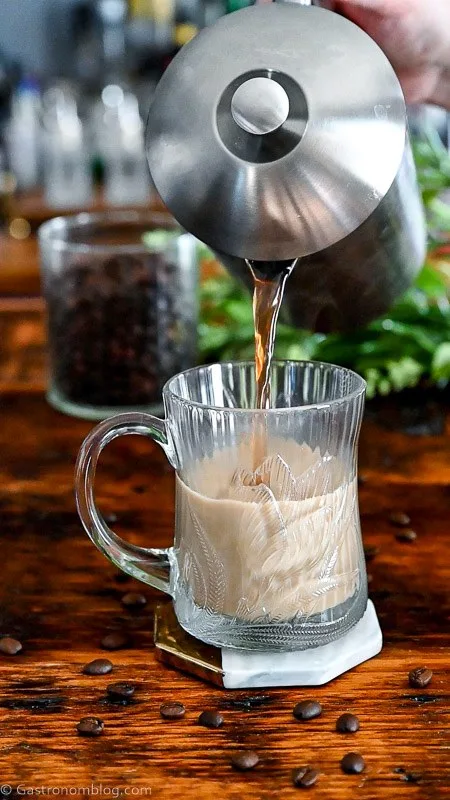 coffee being poured from silver coffee pot into glass mug