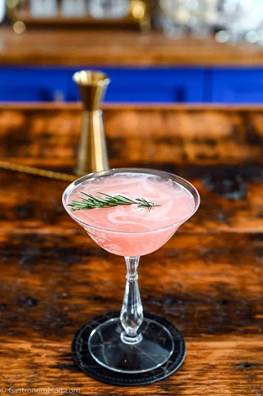 Pink cocktail in cocktail coupe, this Grapefruit Gin cocktail is served on a black coaster on a wooden table