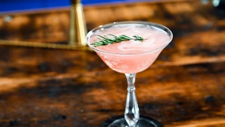 Pink cocktail in cocktail coupe, this Grapefruit Gin cocktail is served on a black coaster on a wooden table