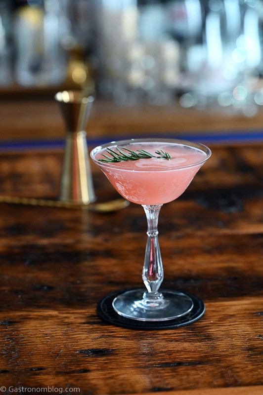 Pink cocktail in cocktail coupe, this Grapefruit Gin cocktail is served on a black coaster on a wooden table