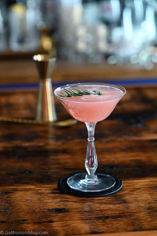 Pink cocktail in cocktail coupe, this Grapefruit Gin cocktail is served on a black coaster on a wooden table