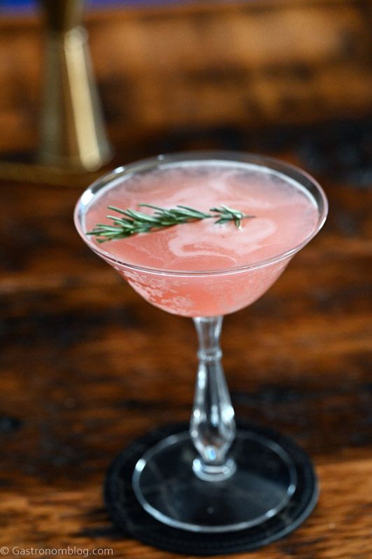 Pink cocktail in cocktail coupe, this Grapefruit Gin cocktail is served on a black coaster on a wooden table