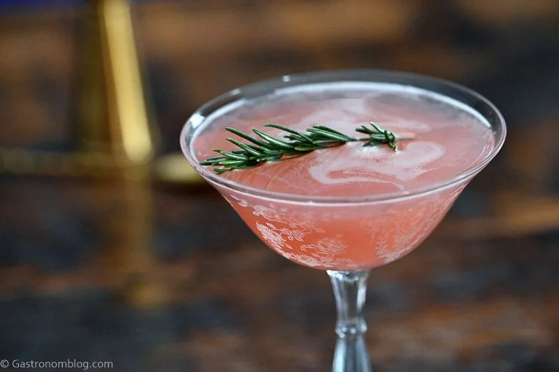 Pink cocktail in cocktail coupe, this Grapefruit Gin cocktail is served on a black coaster on a wooden table