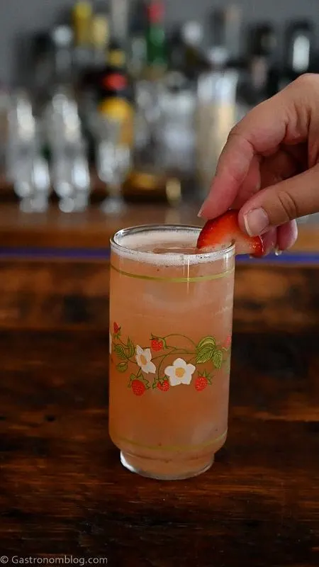 pink Strawberry Vanilla cocktail in strawberry printed vintage glass with hand placing strawberry on rim