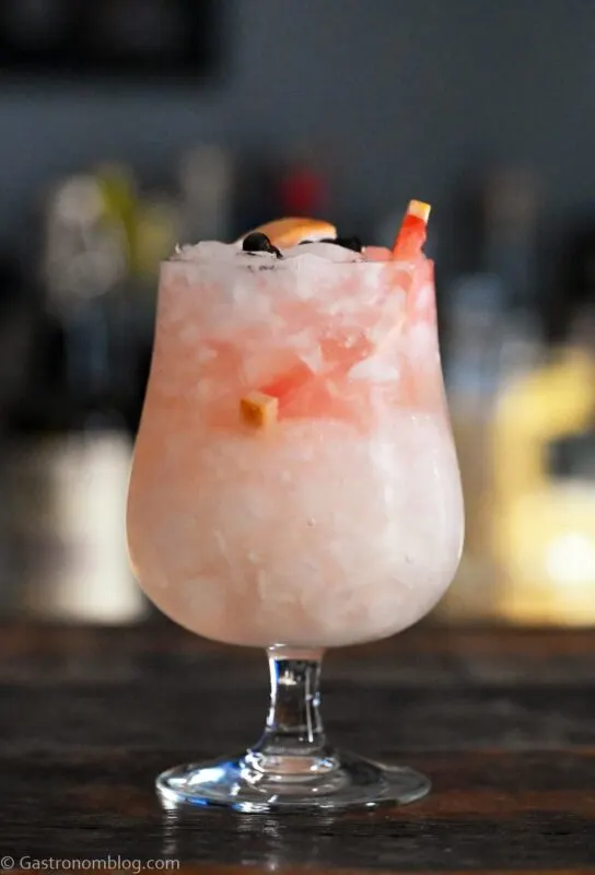 Grapefruit Gin and Tonic in stemmed glass with crushed ice, grapefruit slices and juniper berries on wooden table