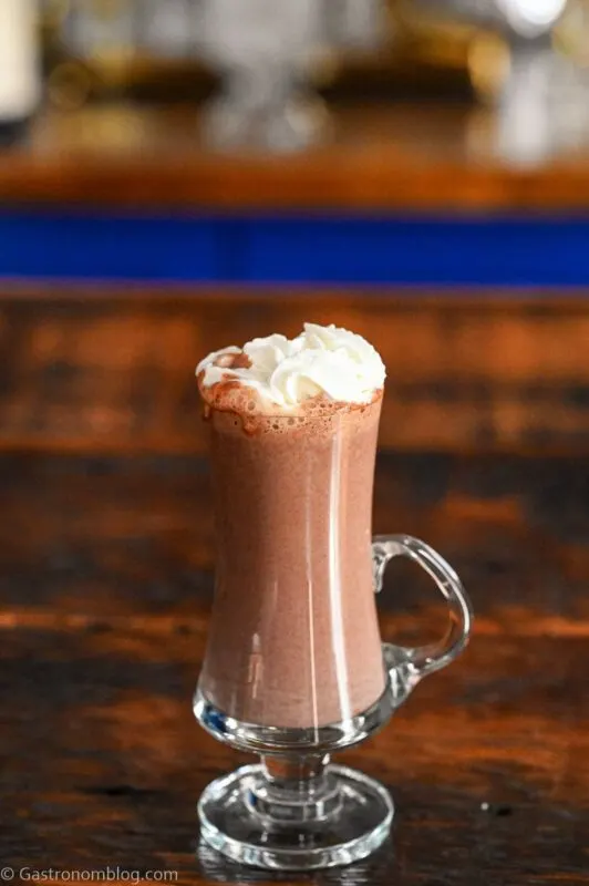 brown peanut butter hot chocolate in glass mug with whipped cream on top on wooden table