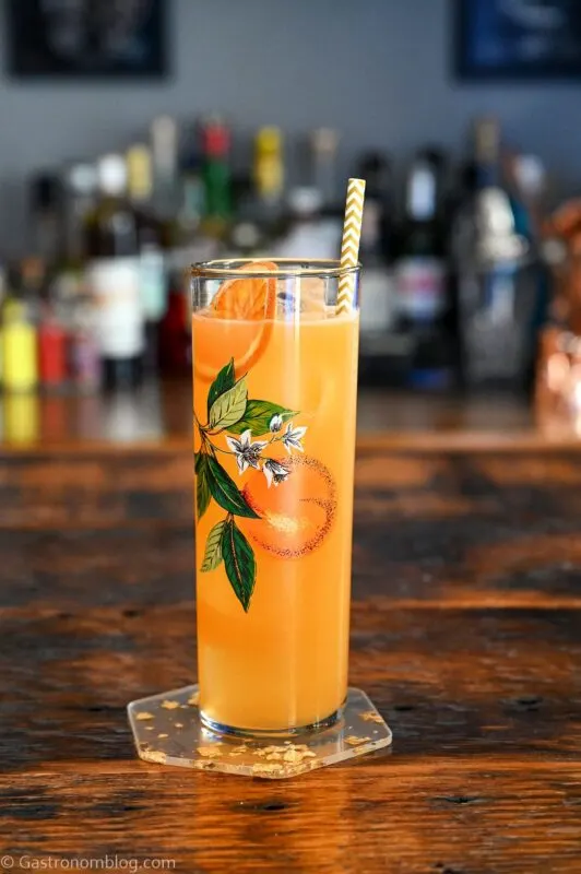orange colored Irn Bru cocktail in orange patterned highball glass with straw. On wooden table