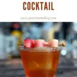 brown cocktail in rocks glass with rhubarb slice garnish on pick. Glass is on a coaster on a wooden table.