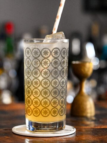 orange and white colored Earl Grey Collins cocktail in gray circle printed highball glass, on white coaster on wooden table