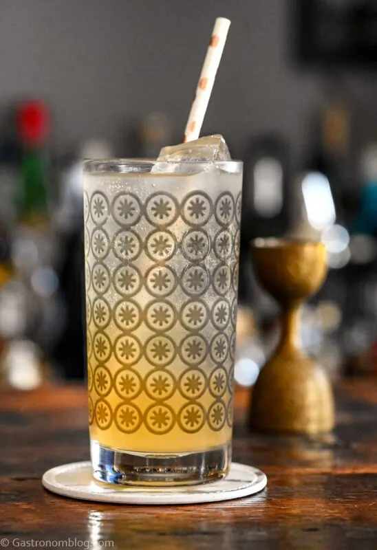 orange and white colored Earl Grey Collins cocktail in gray circle printed highball glass, on white coaster on wooden table