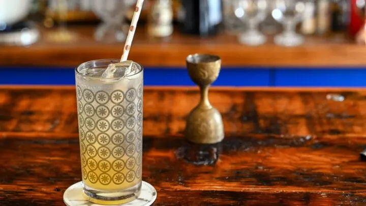 orange and white colored Earl Grey Collins cocktail in gray circle printed highball glass, on white coaster on wooden table
