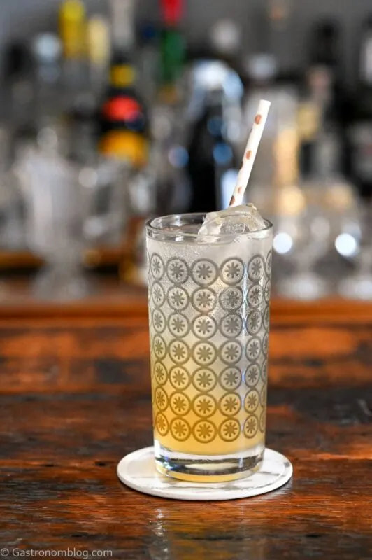 orange and white colored Earl Grey Collins cocktail in gray circle printed highball glass, on white coaster on wooden table