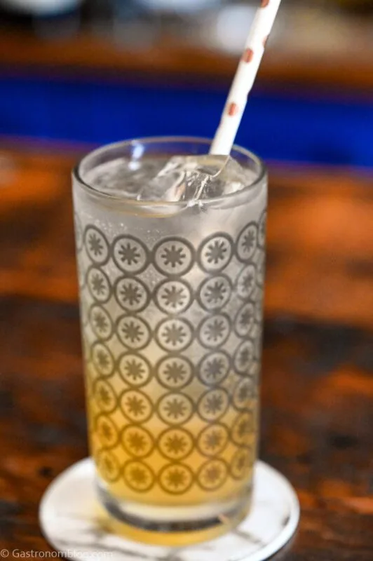 orange and white colored Earl Grey Collins cocktail in gray circle printed highball glass, on white coaster on wooden table