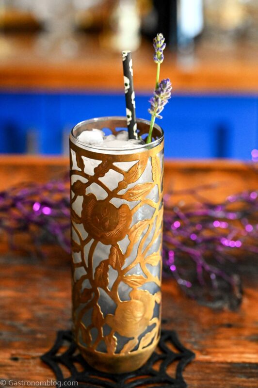Midnight Margaritas in Metal chased floral tumblers with skull straw, lavender garnishes on wooden table