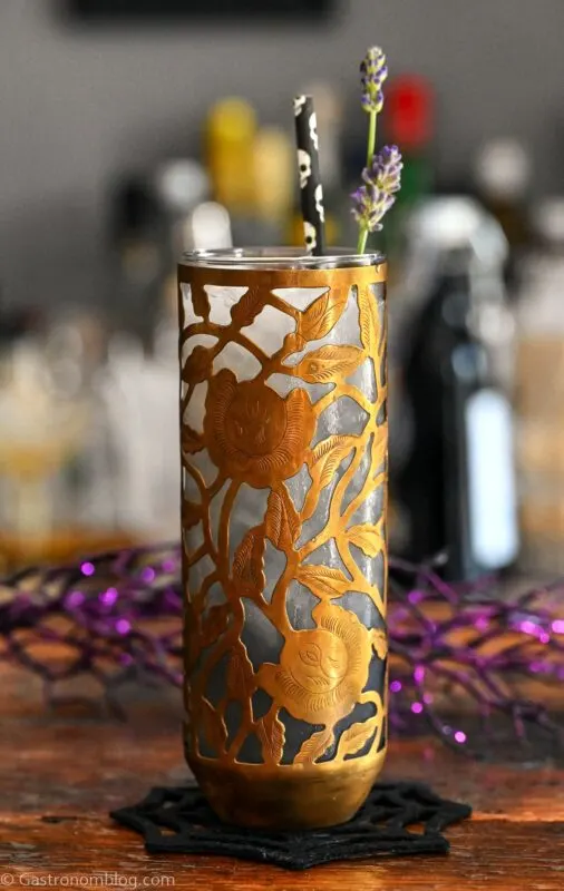 Midnight Margaritas in Metal chased floral tumblers with skull straw, lavender garnishes on wooden table