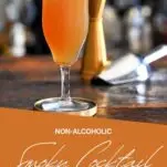 Orange colored Smoky mocktail in tall cocktail coupe with foam on white and gold coaster on wooden table