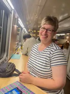 woman in striped shirt seated on stool in club car on Caledonian Sleeper Train