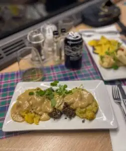 neeps and tatties and meat on white plate on tartan placemat on Caledonian Sleeper Train