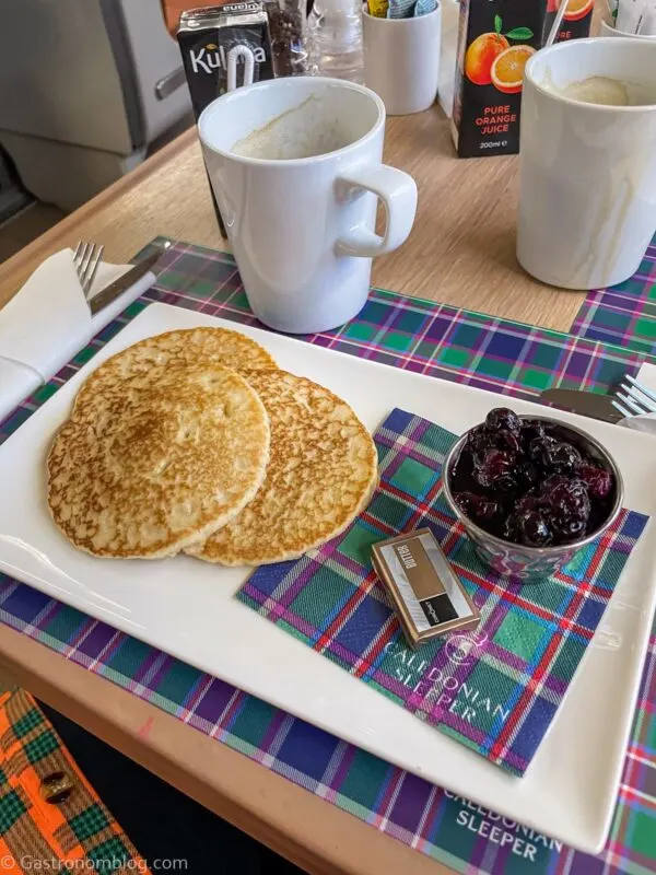 breakfast pancakes and berry compote on white plate and tartan placemat in club car on Caledonian Sleeper Train