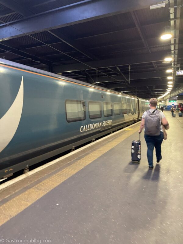 green Caledonian Sleeper Train in Eustan Train Station in London, lady walking with luggage