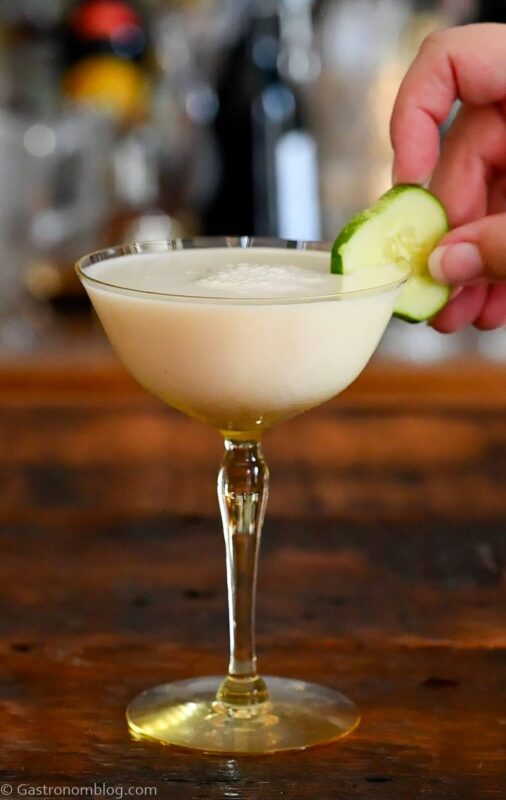 yellow cocktail glass with white yogurt cocktail and cucumber and mint garnish