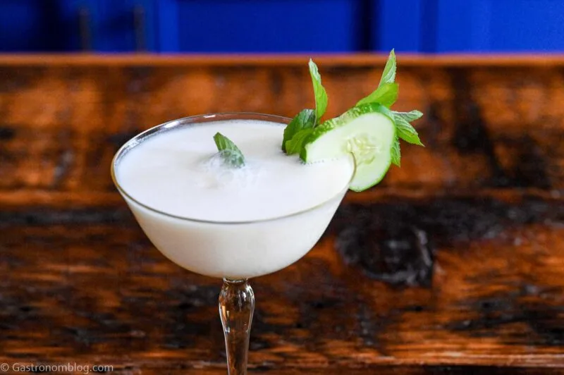 yellow cocktail glass with white yogurt cocktail and cucumber and mint garnish