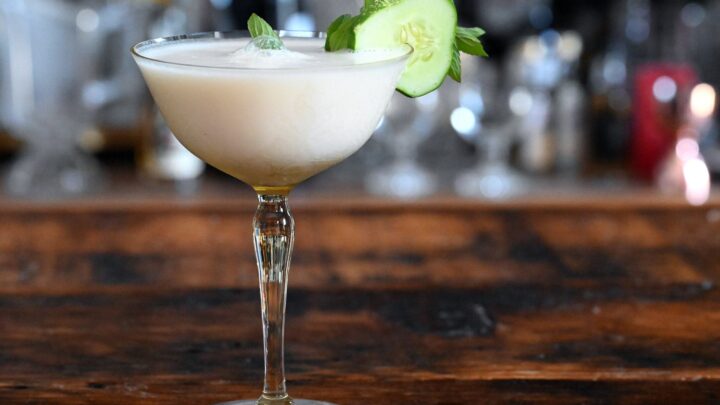 yellow cocktail glass with white yogurt cocktail and cucumber and mint garnish