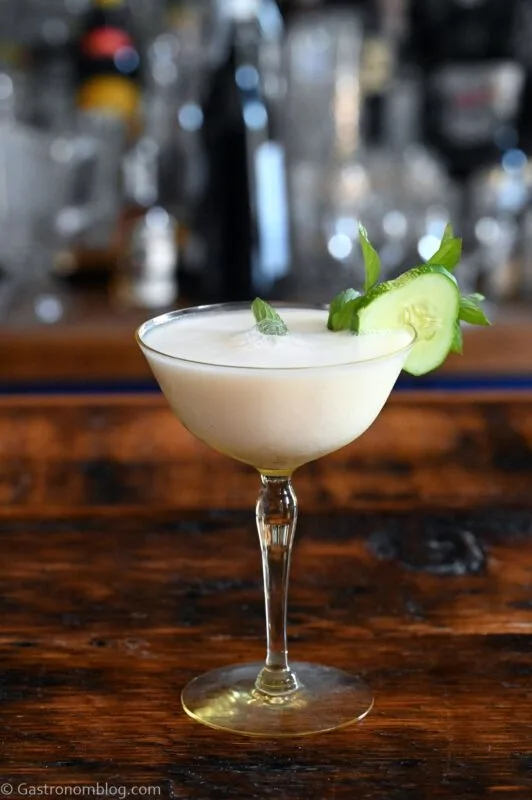 yellow cocktail glass with white yogurt cocktail and cucumber and mint garnish