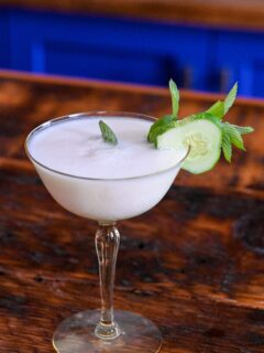 yellow cocktail glass with white yogurt cocktail and cucumber and mint garnish