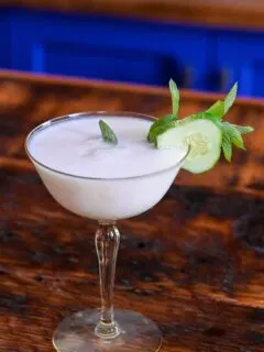 yellow cocktail glass with white yogurt cocktail and cucumber and mint garnish