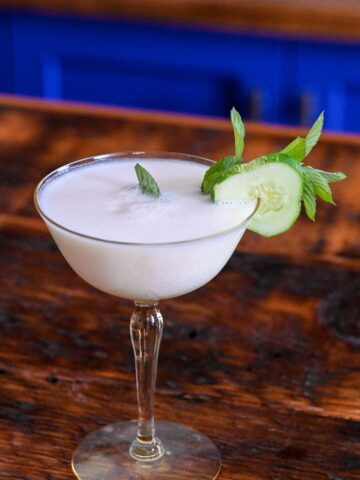 yellow cocktail glass with white yogurt cocktail and cucumber and mint garnish
