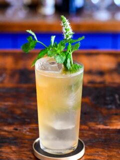 tan Earl Grey Gin Cocktail in tumbler with mint sprig garnish on wooden table