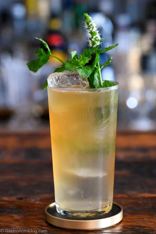 tan Earl Grey Gin Cocktail in tumbler with mint sprig garnish on wooden table