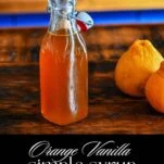 Orange Vanilla Simple Syrup in bottle. Oranges next to bottle on wooden table.