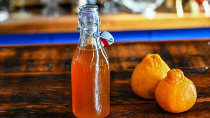 Orange Vanilla Simple Syrup in bottle. Oranges next to bottle on wooden table.