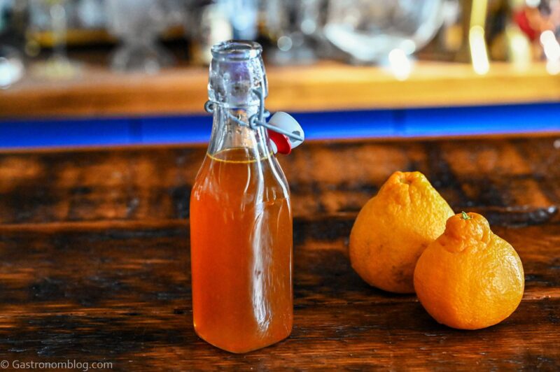 Orange Vanilla Simple Syrup in bottle. Oranges next to bottle on wooden table.