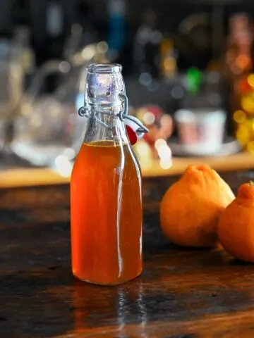 Orange Vanilla Simple Syrup in bottle. Oranges next to bottle on wooden table.