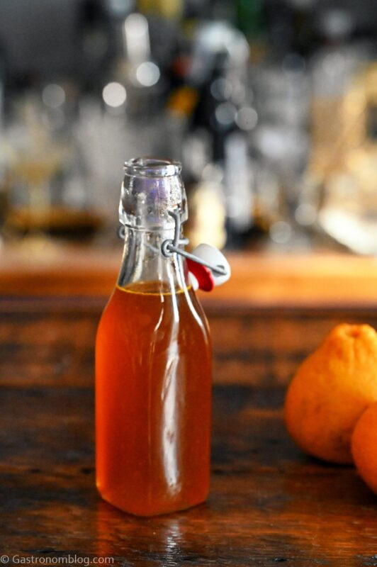 Orange Vanilla Simple Syrup in bottle. Oranges next to bottle on wooden table.