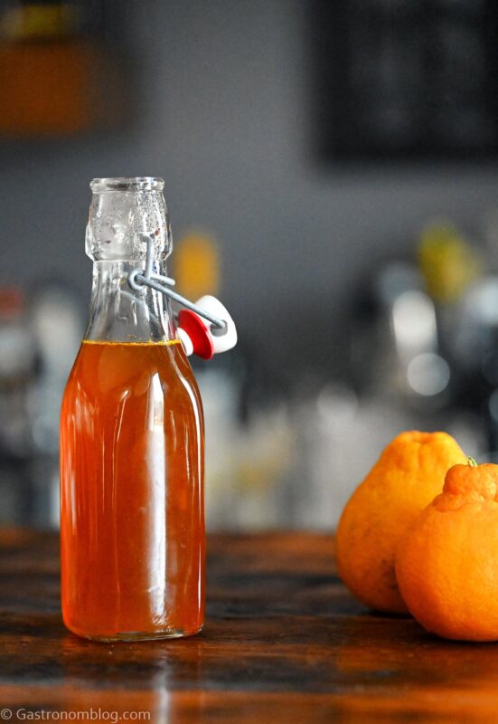 Orange Vanilla Simple Syrup in bottle. Oranges next to bottle on wooden table.
