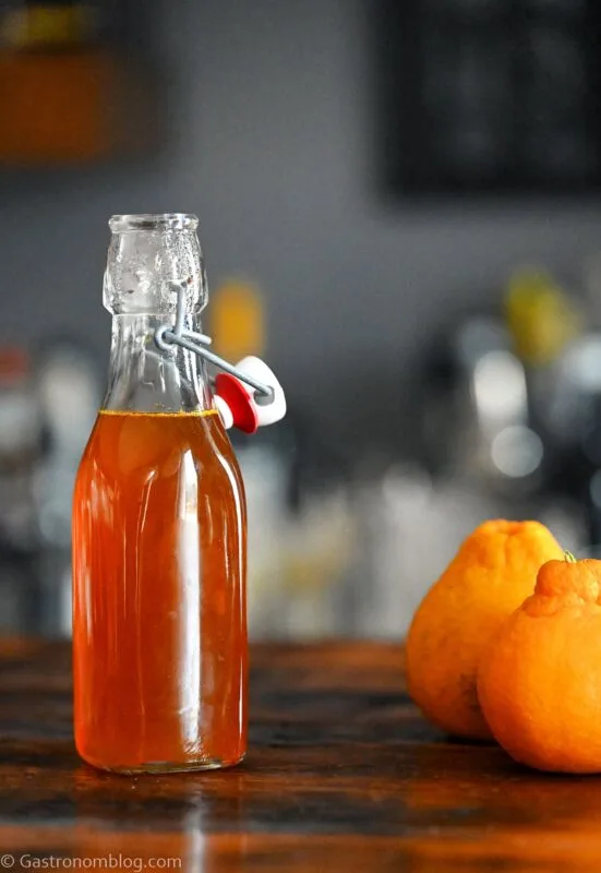 Orange Vanilla Simple Syrup in bottle. Oranges next to bottle on wooden table.