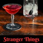 red Stranger Things Drink with dried dragonfruit chip garnish in cocktail coupe on wooden table with black background