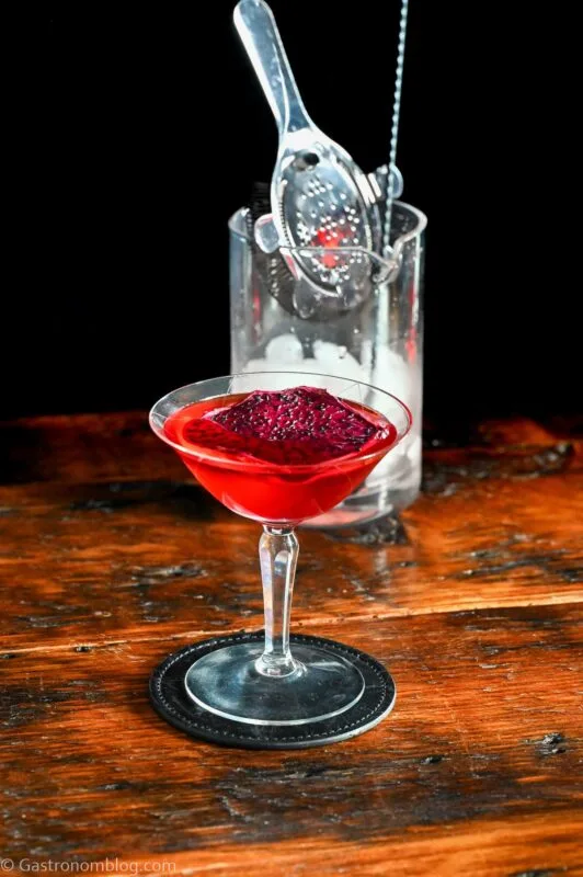 red Stranger Things Drink with dried dragonfruit chip garnish in cocktail coupe on wooden table with black background