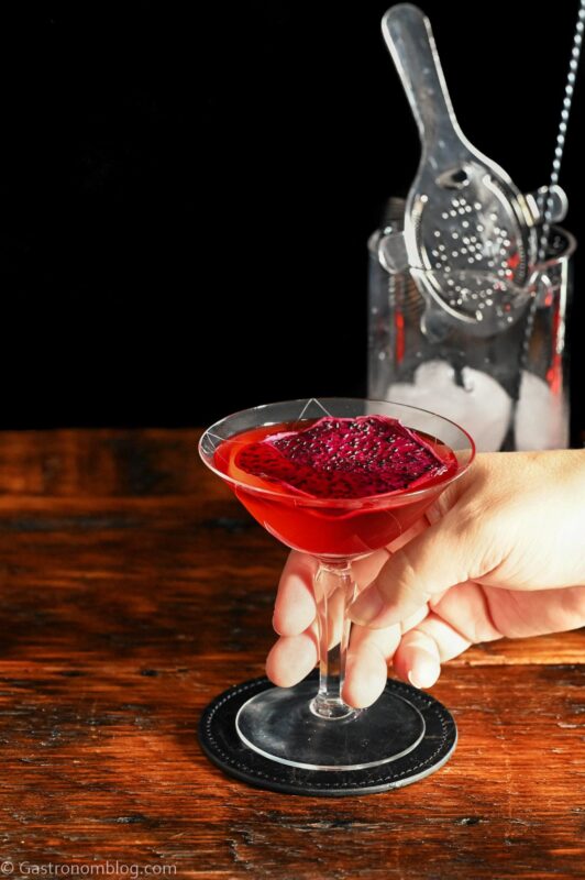 red Stranger Things Drink with dried dragonfruit chip garnish in cocktail coupe on wooden table with black background