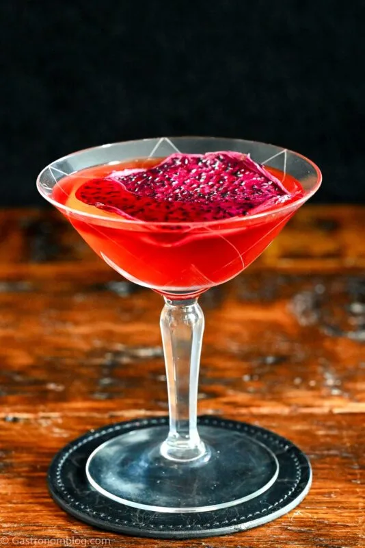 red Stranger Things Drink with dried dragonfruit chip garnish in cocktail coupe on wooden table with black background