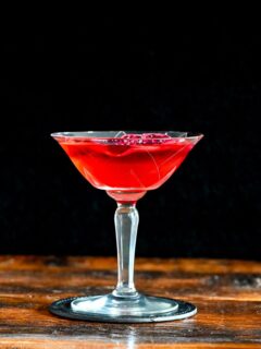 red Stranger Things Drink with dried dragonfruit chip garnish in cocktail coupe on wooden table with black background