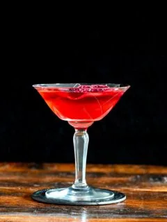 red Stranger Things Drink with dried dragonfruit chip garnish in cocktail coupe on wooden table with black background