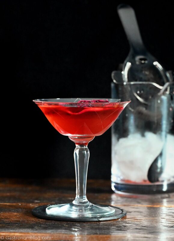 red Stranger Things Drink with dried dragonfruit chip garnish in cocktail coupe on wooden table with black background