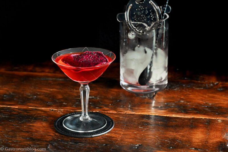 red Stranger Things Drink with dried dragonfruit chip garnish in cocktail coupe on wooden table with black background
